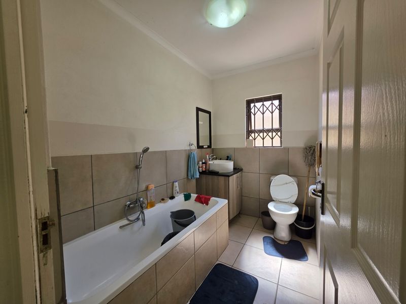 A functional bathroom featuring a bathtub with shower mixer, a vanity cabinet with vessel sink, and a toilet, finished with neutral wall and floor tiles.
