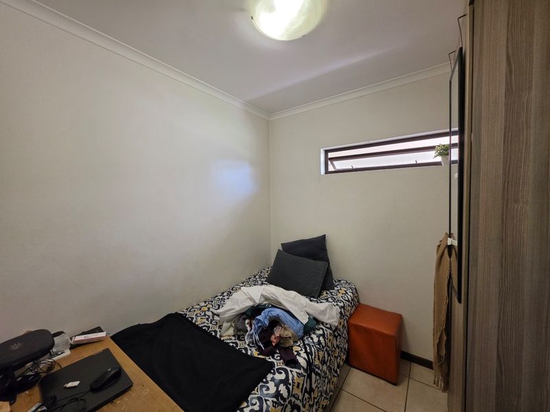 A compact bedroom featuring tiled flooring, a built-in wardrobe, and a high-level window providing natural light.
