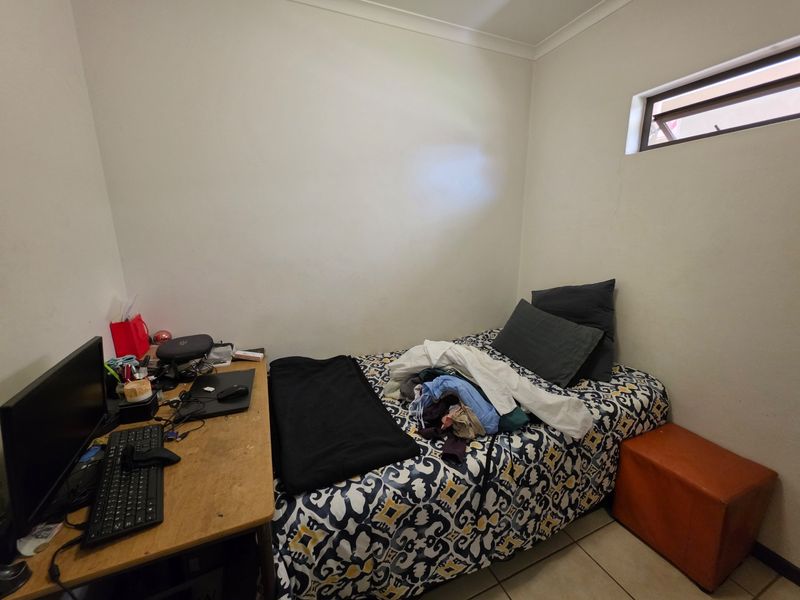 A compact bedroom featuring tiled flooring and a high-level window, providing a functional space suitable for a single bed and workspace.