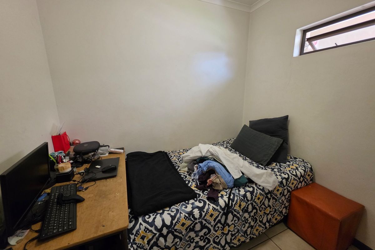 A compact bedroom featuring tiled flooring and a high-level window, providing a functional space suitable for a single bed and workspace.