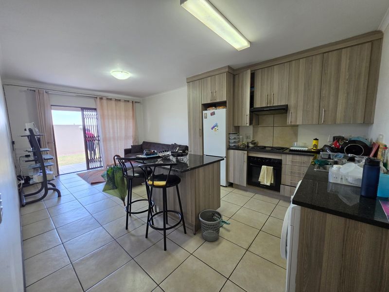 Open-plan living area featuring a kitchen with granite countertops, built-in oven, and hob, flowing into a lounge space with access to an outdoor patio.