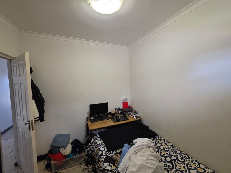 A compact bedroom featuring tiled flooring, white walls, and a simple flush mount ceiling light, offering a functional space for rest or study.