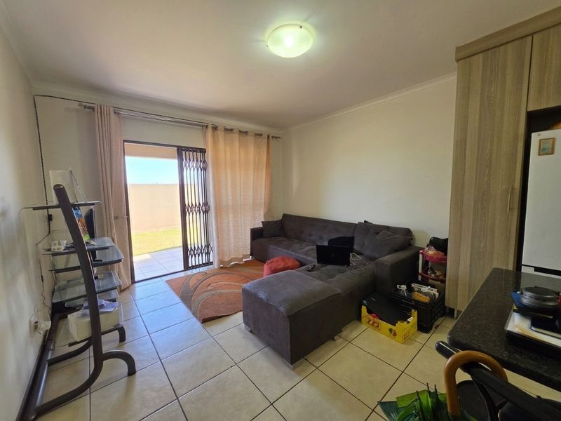 A living room featuring tiled flooring and a sliding glass door with a security gate, providing direct access to an outdoor patio area.