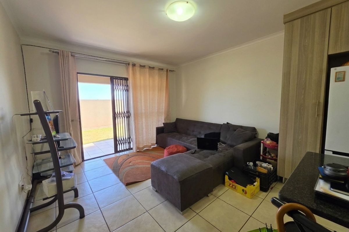 A living room featuring tiled flooring and a sliding glass door with a security gate, providing direct access to an outdoor patio area.
