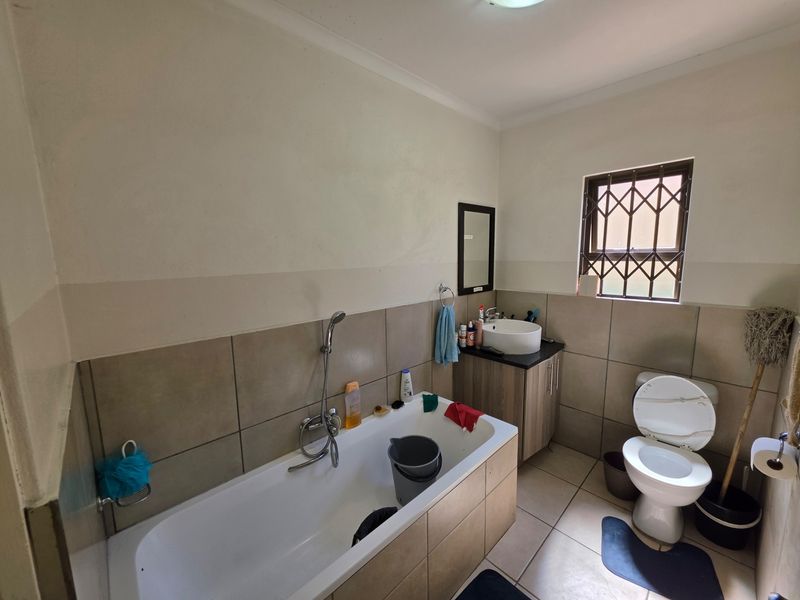 A functional bathroom featuring a bathtub with handheld shower, a vanity with vessel sink, and a toilet, finished with neutral wall and floor tiles.