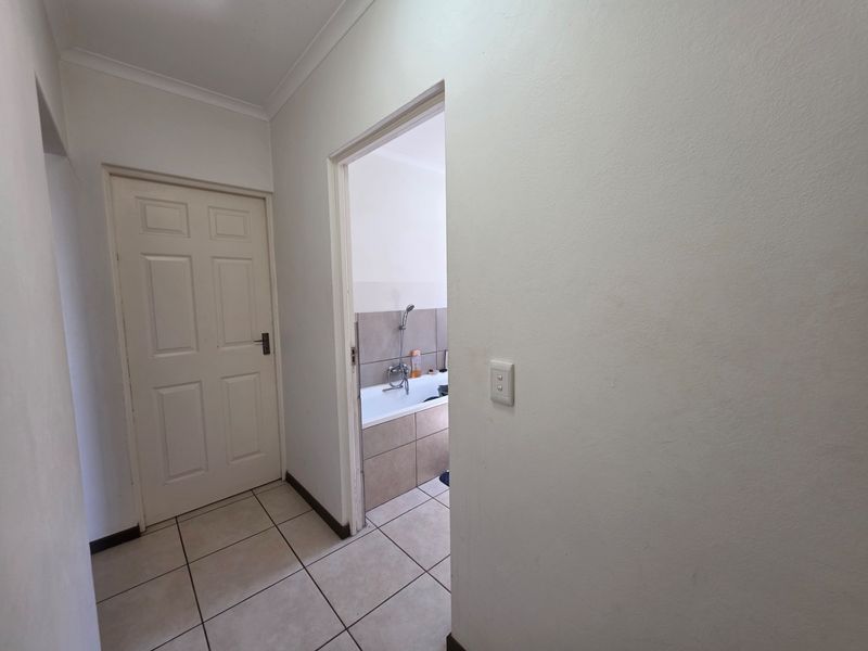 A clean, neutral hallway featuring tiled flooring and coved cornicing, providing access to an adjacent bathroom.