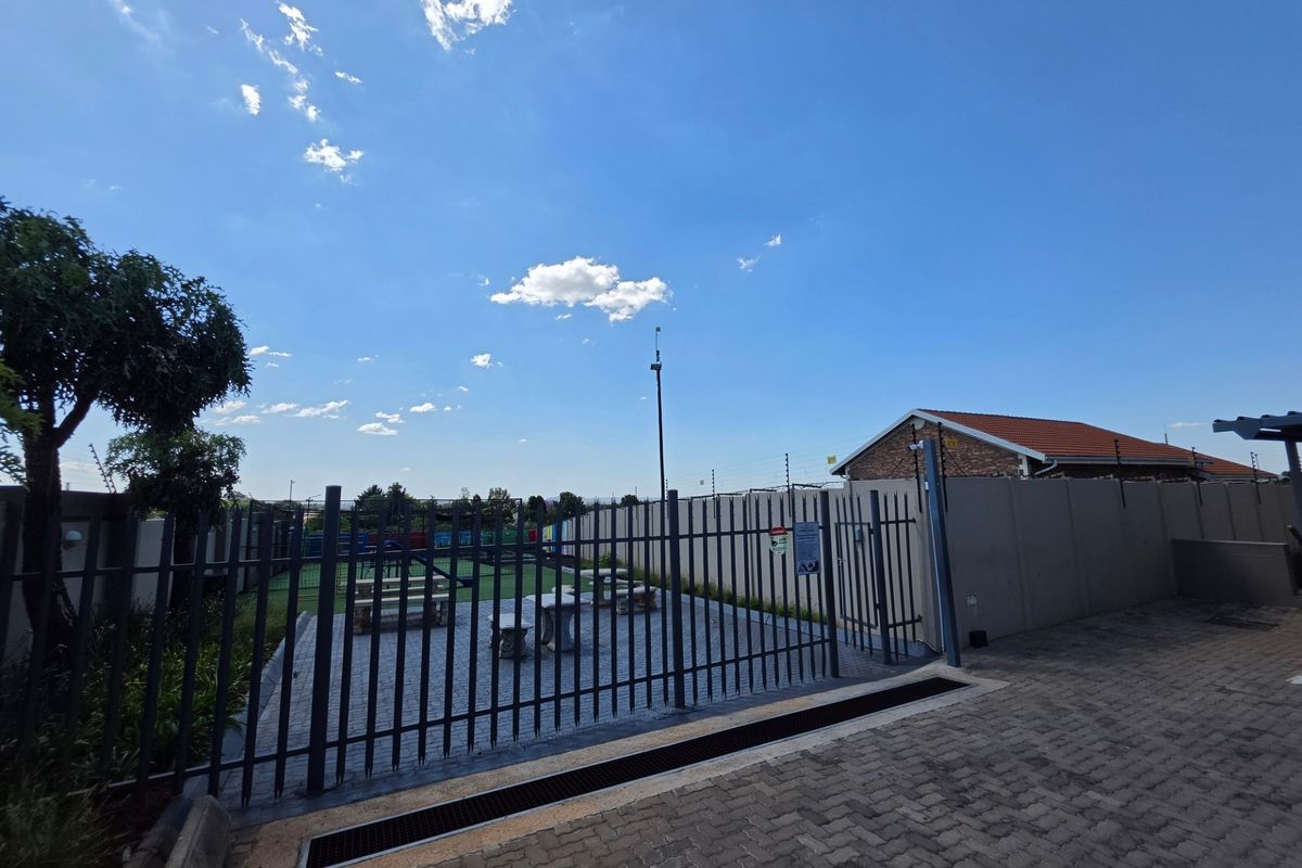 A secure outdoor communal area featuring paved patio space, perimeter walling with electric fencing, and drainage infrastructure.
