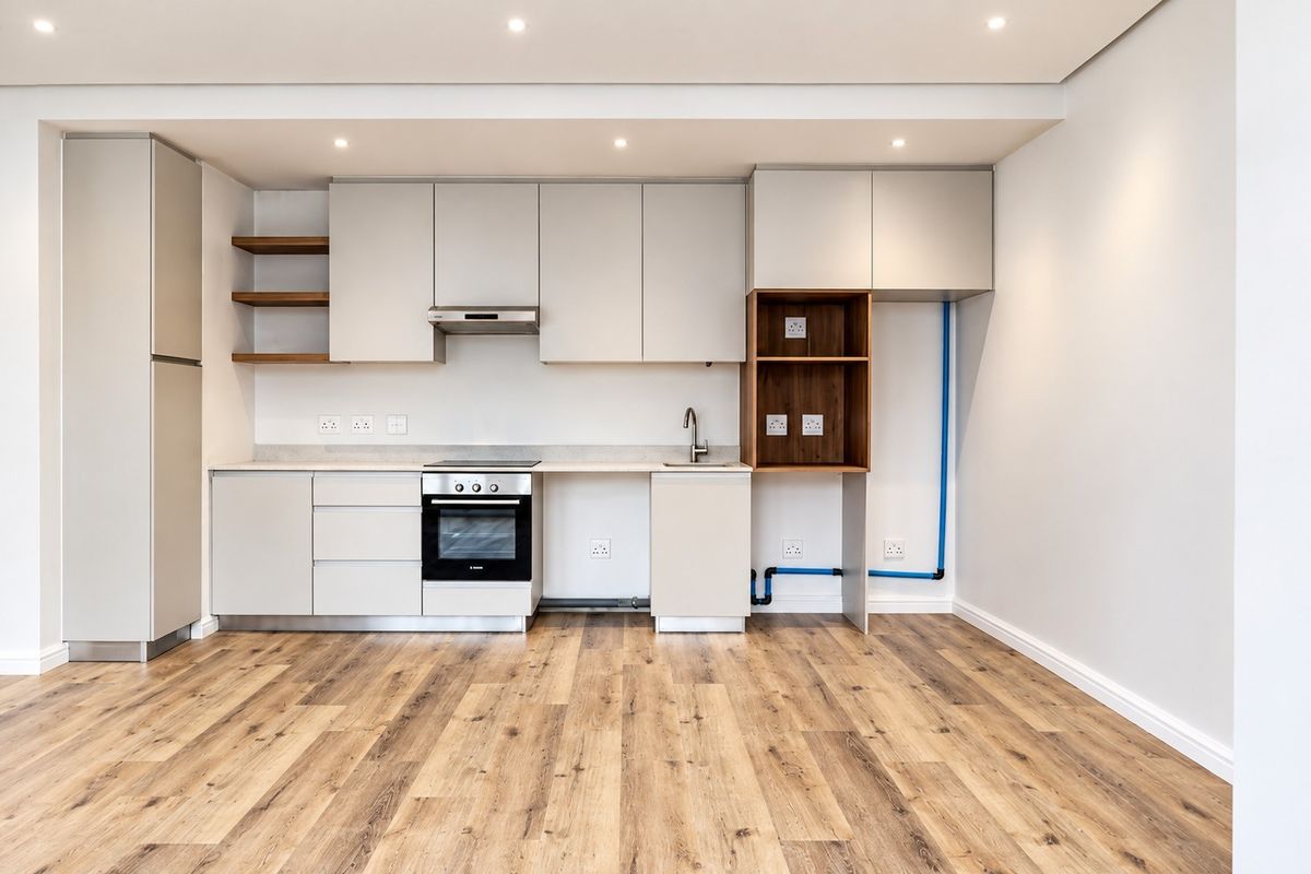 Modern kitchen featuring sleek cabinetry, integrated oven, extractor fan, and wood-look laminate flooring. The space is clean and ready for final appliance installation.