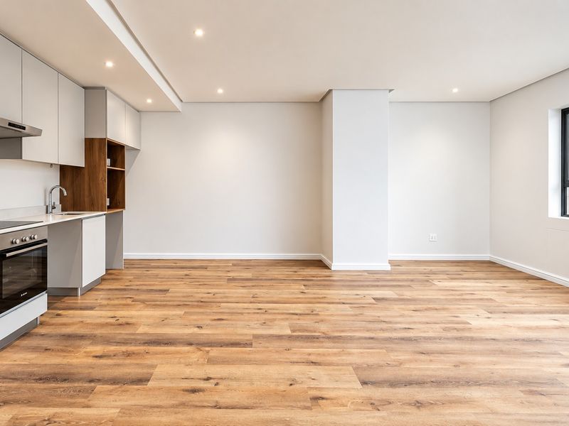 A bright, modern open-plan living and kitchen area featuring sleek cabinetry, integrated appliances, recessed lighting, and high-quality wood-look laminate flooring.