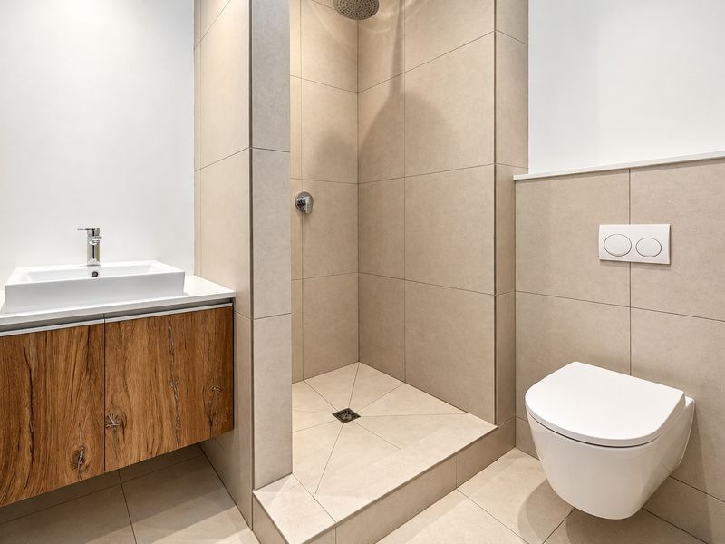 Modern bathroom featuring a wall-mounted wood-finish vanity, walk-in shower with rain head, and a sleek wall-hung toilet with concealed cistern.