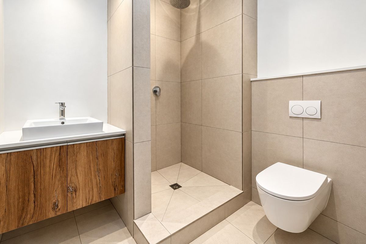 Modern bathroom featuring a wall-mounted wood-finish vanity, walk-in shower with rain head, and a sleek wall-hung toilet with concealed cistern.