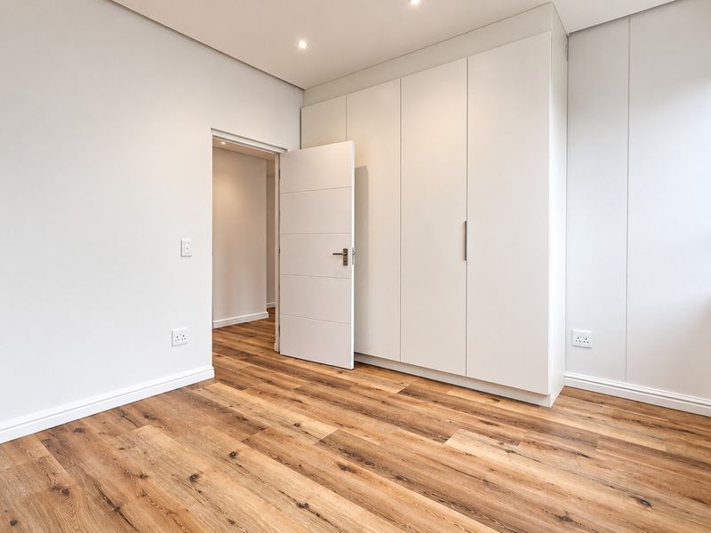 A bright, modern bedroom featuring high-quality laminate flooring, ample built-in cupboard space, and clean, neutral finishes throughout.