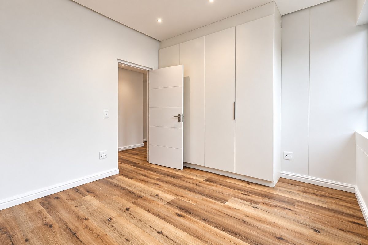 A bright, modern bedroom featuring high-quality laminate flooring, ample built-in cupboard space, and clean, neutral finishes throughout.
