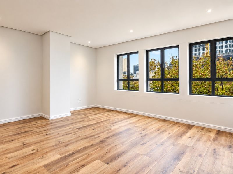 A bright and spacious living area featuring modern laminate timber flooring, recessed downlights, and large windows with urban views.