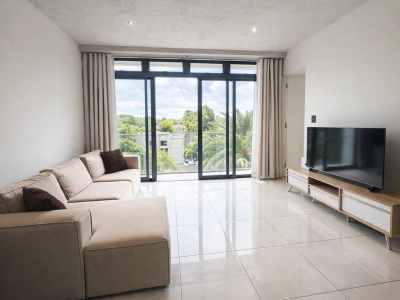 Bright and modern living room featuring large sliding glass doors that open to a balcony, complemented by polished tiled flooring and recessed lighting.