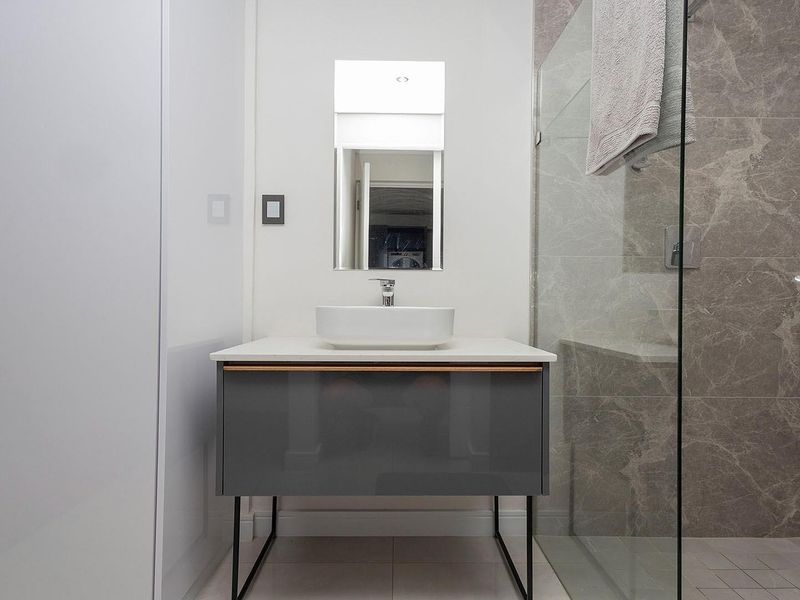 Modern bathroom featuring a floating vanity with vessel sink, glass-enclosed shower, and elegant marble-effect wall tiling.