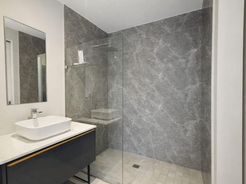 Modern bathroom featuring a walk-in shower with rain shower head, marble-look wall tiles, and a contemporary vanity with a countertop basin.