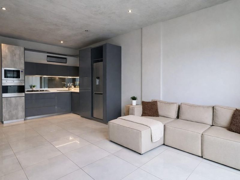 Modern open-plan living area featuring a sleek kitchen with integrated appliances, high-gloss cabinetry, mirrored splashback, and polished tiled flooring throughout.