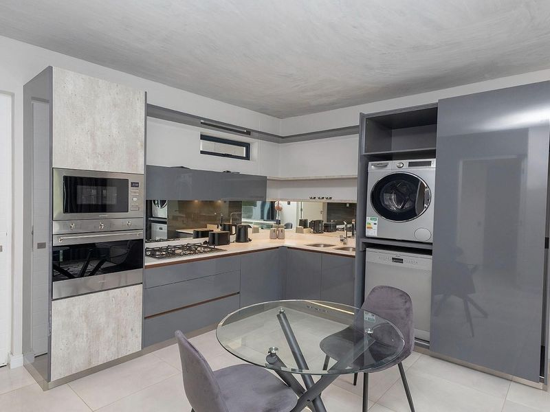 Modern kitchen featuring high-gloss cabinetry, integrated appliances including a laundry unit and dishwasher, stone countertops, and a sleek mirror splashback.