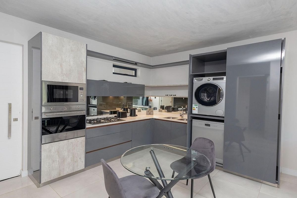 Modern kitchen featuring high-gloss cabinetry, integrated appliances including a laundry unit and dishwasher, stone countertops, and a sleek mirror splashback.