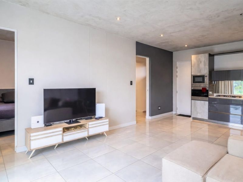 Modern open-plan living area featuring tiled flooring, recessed lighting, and a sleek kitchen with integrated appliances and contemporary cabinetry.