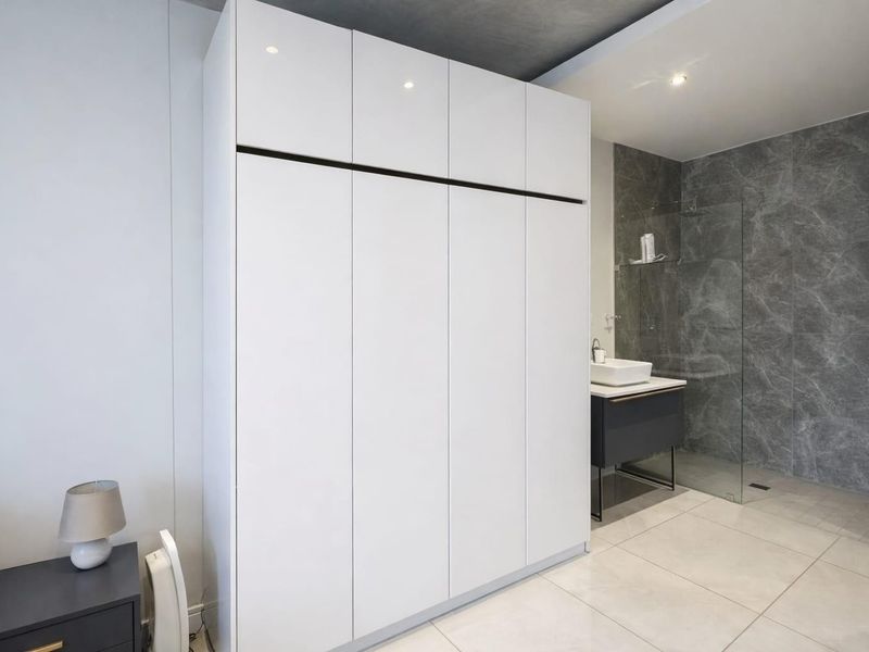 Modern bedroom featuring a large built-in wardrobe and an integrated en-suite bathroom with a glass shower screen and contemporary vanity.