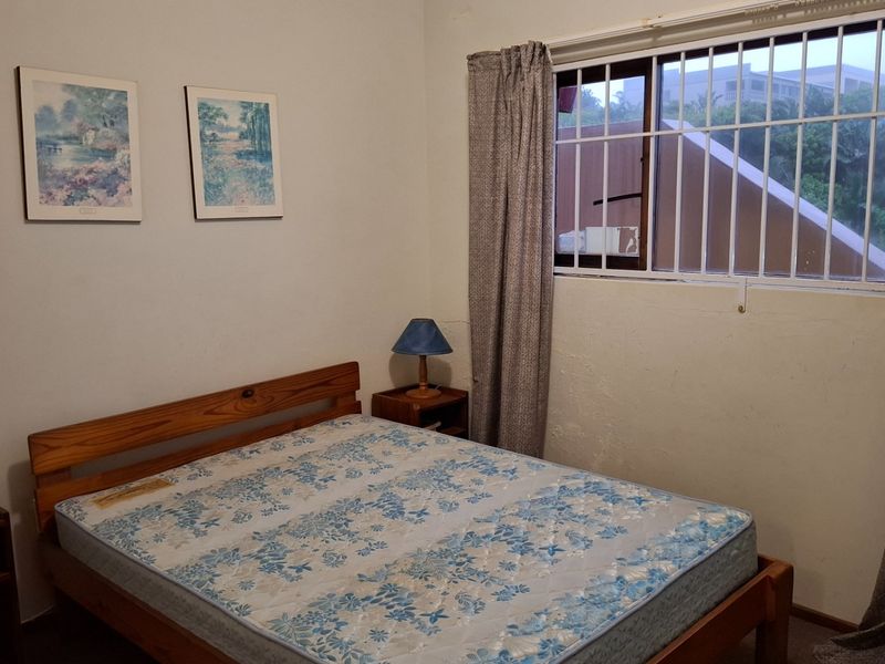 A bedroom featuring a window with security bars and visible wall surface wear, offering a functional space ready for cosmetic updates.