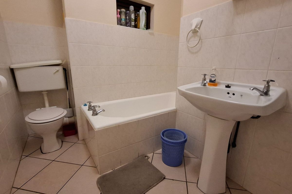 A functional bathroom featuring a pedestal washbasin, bathtub, and toilet with neutral wall and floor tiling.