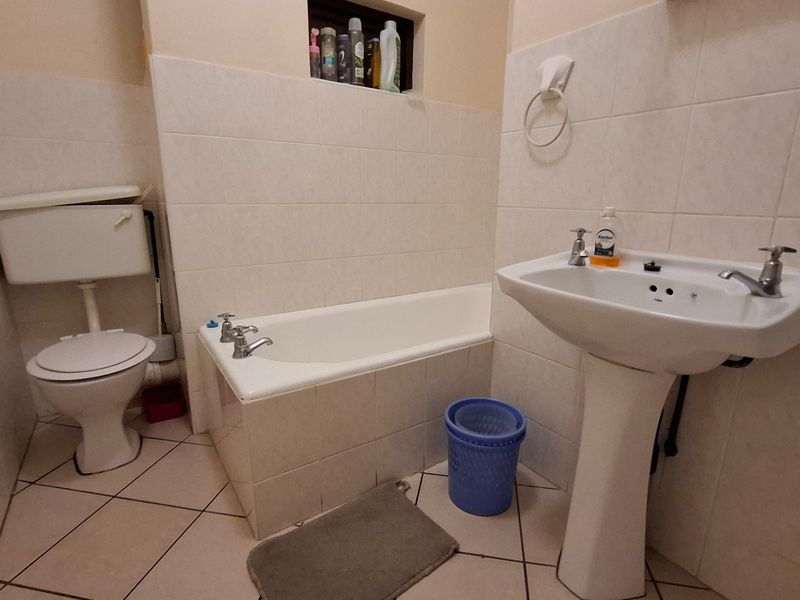A functional bathroom featuring a pedestal washbasin, bathtub, and toilet with neutral wall and floor tiling.