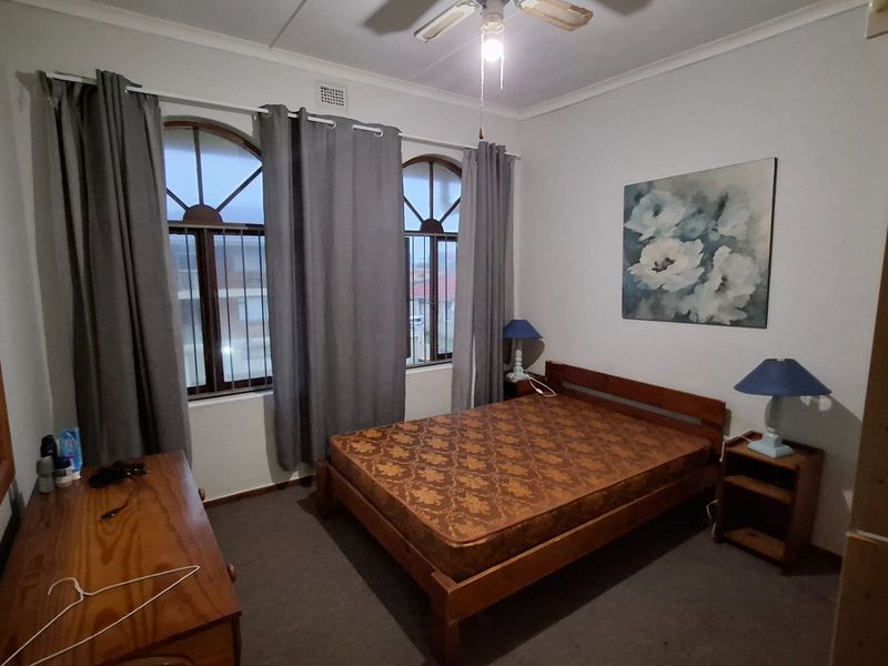 A bedroom featuring arched windows with security bars, carpeted flooring, and a ceiling fan.