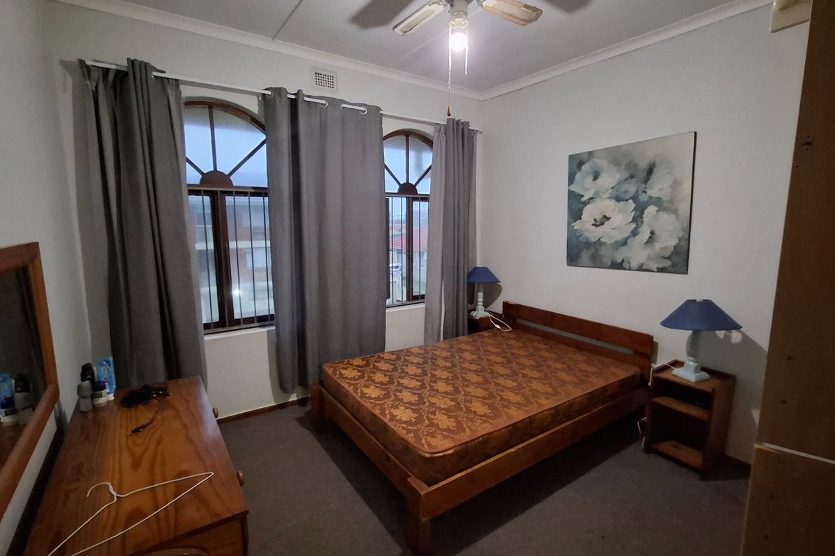 A bedroom featuring arched windows with security bars, carpeted flooring, and a ceiling fan.