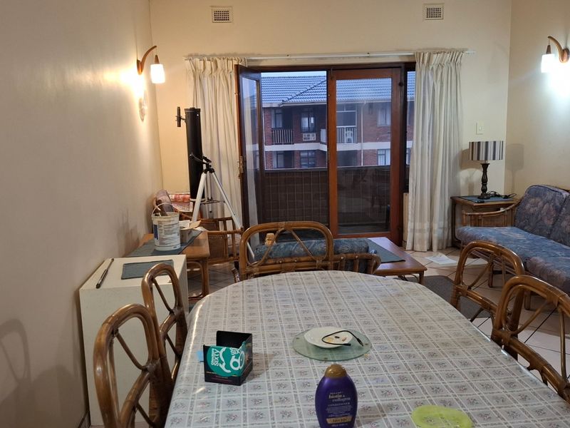 A living and dining area featuring tiled floors, wall-mounted lighting, and direct access to a balcony through sliding glass doors.