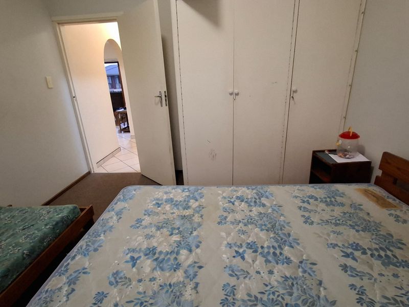 A bedroom featuring built-in cupboards with visible wear, providing access to an adjacent hallway.
