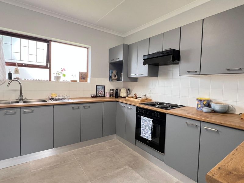 Modern kitchen featuring grey cabinetry, wooden countertops, tiled backsplash, and integrated appliances including an oven, hob, and extractor fan.