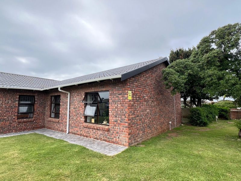 A well-maintained single-story face brick house featuring a tiled roof, aluminium window frames, and a neat paved walkway set within a landscaped garden.