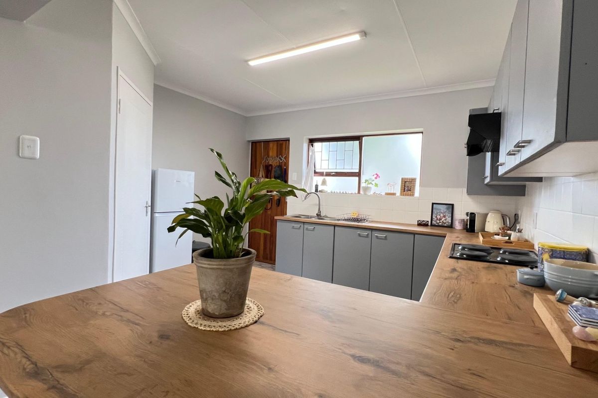 A functional kitchen featuring modern grey cabinetry, wood-look laminate countertops, a built-in hob, and a tiled splashback with ample natural light.