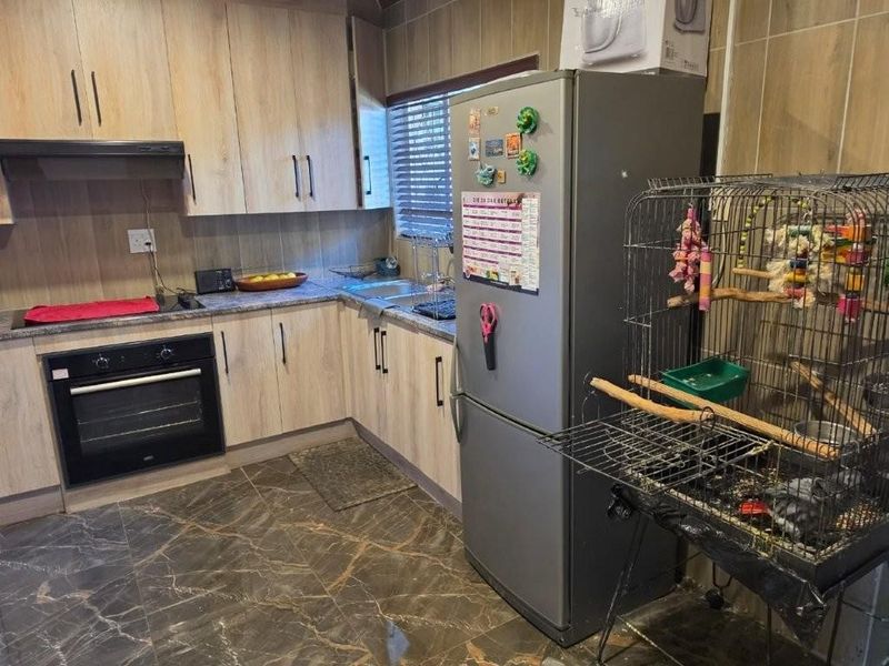 A functional kitchen featuring light wood-finish cabinetry, dark marble-effect floor tiles, integrated oven and hob, and a tiled backsplash.