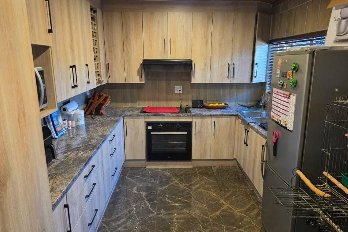 A functional kitchen featuring wood-look cabinetry, stone-patterned countertops, integrated oven and hob, and durable tiled flooring.