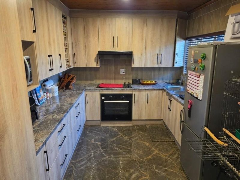 A functional kitchen featuring wood-look cabinetry, stone-patterned countertops, integrated oven and hob, and durable tiled flooring.