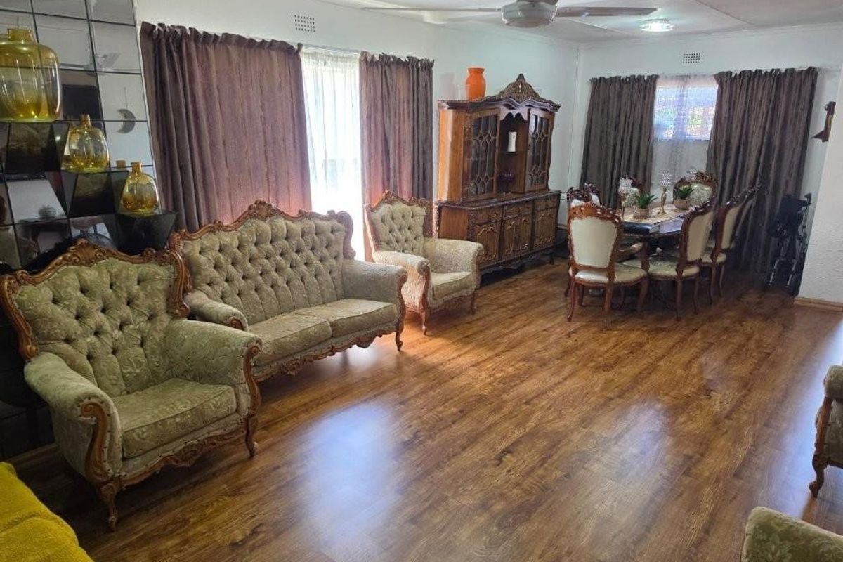 Spacious living and dining area featuring laminate flooring, a ceiling fan, and decorative mirrored wall paneling.