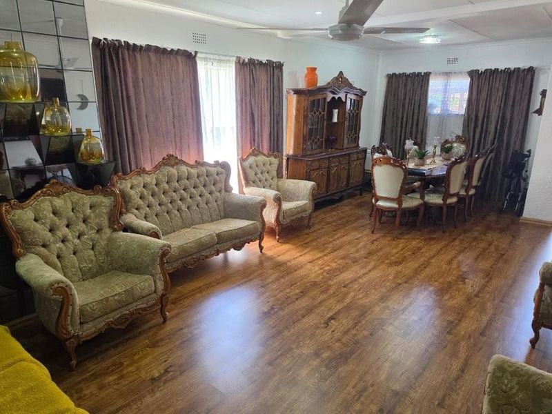 Spacious living and dining area featuring laminate flooring, a ceiling fan, and decorative mirrored wall paneling.