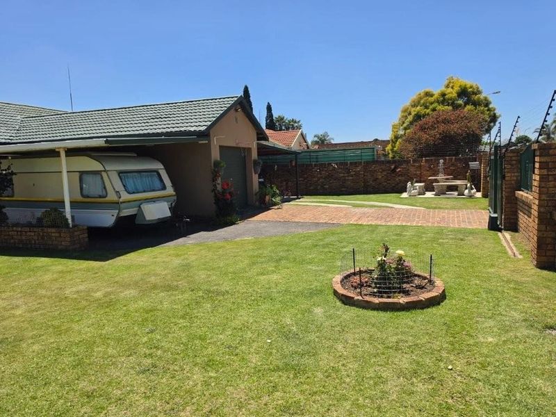 A well-maintained rear garden featuring a paved driveway, carport, and brick boundary wall with electric fencing.
