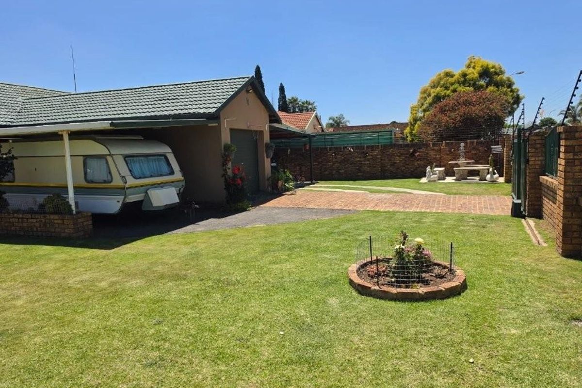 A well-maintained rear garden featuring a paved driveway, carport, and brick boundary wall with electric fencing.