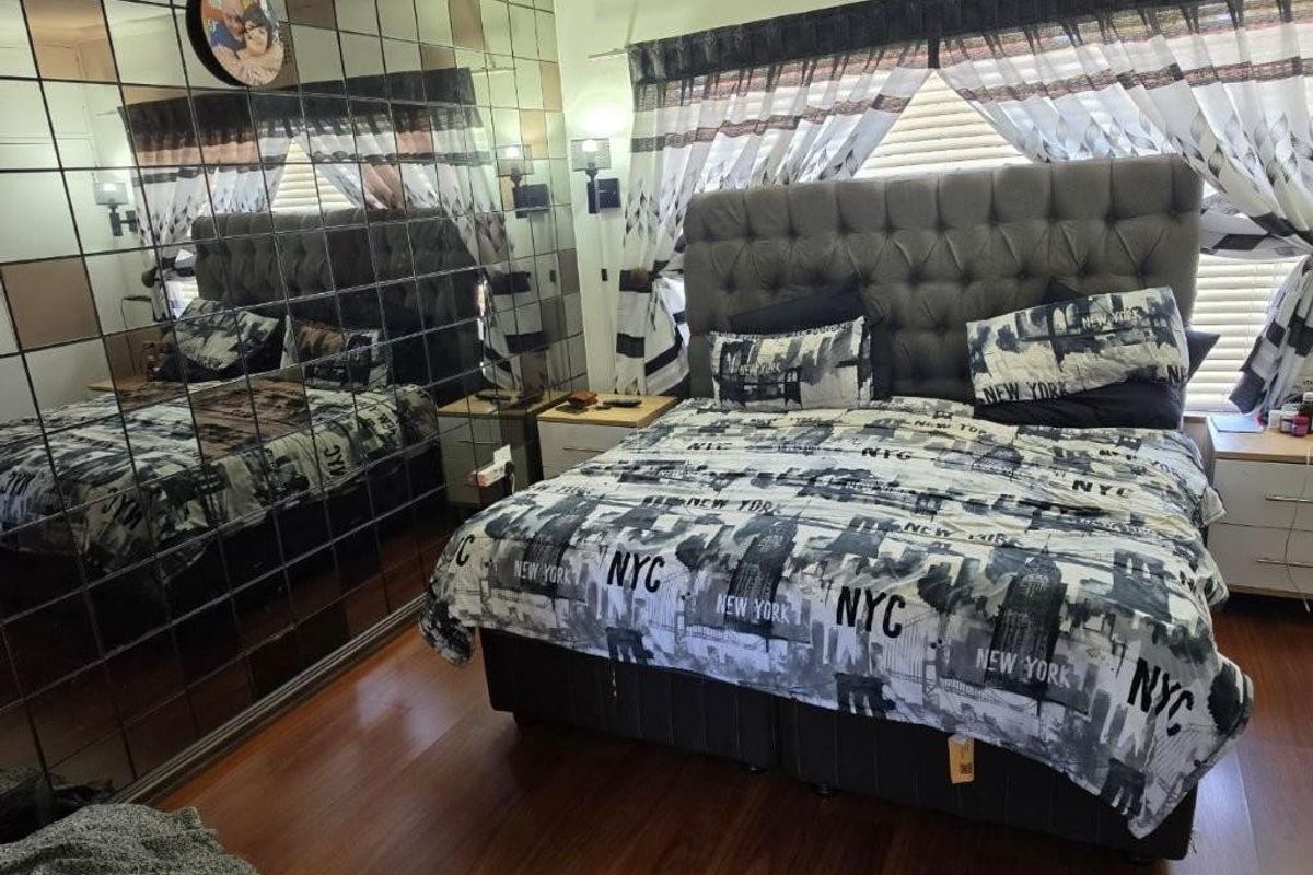A bedroom featuring a large mirrored feature wall, laminate flooring, and built-in wall lighting.