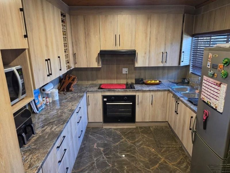 A functional kitchen featuring light wood-look cabinetry, dark stone-effect countertops, built-in oven and hob, and polished dark floor tiles.