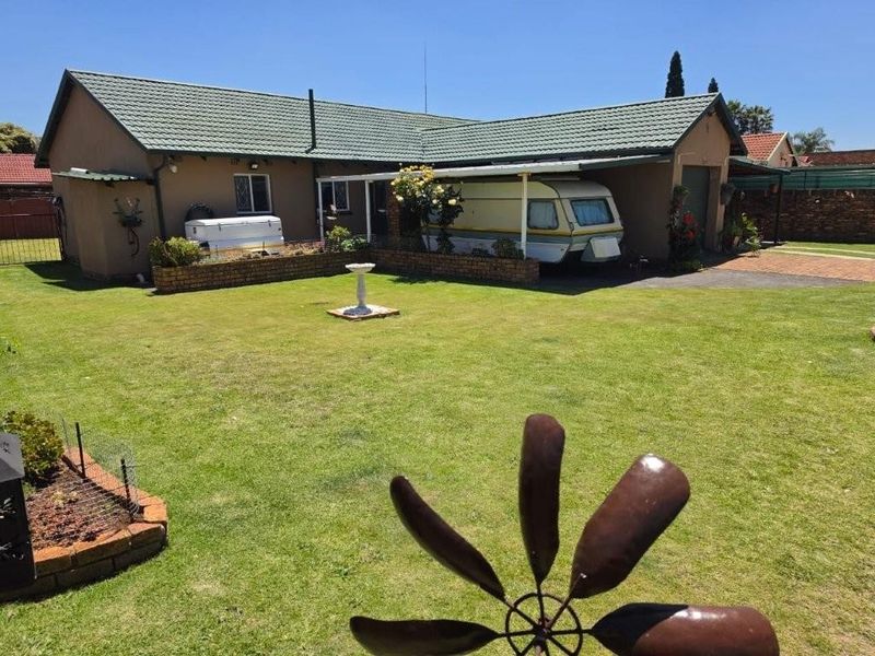 Rear view of the property featuring a spacious lawn, brick retaining wall, and a covered carport area adjacent to the garage.