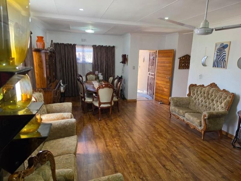 Spacious open-plan living and dining area featuring warm laminate flooring, a ceiling fan, and direct access to an exterior entrance.