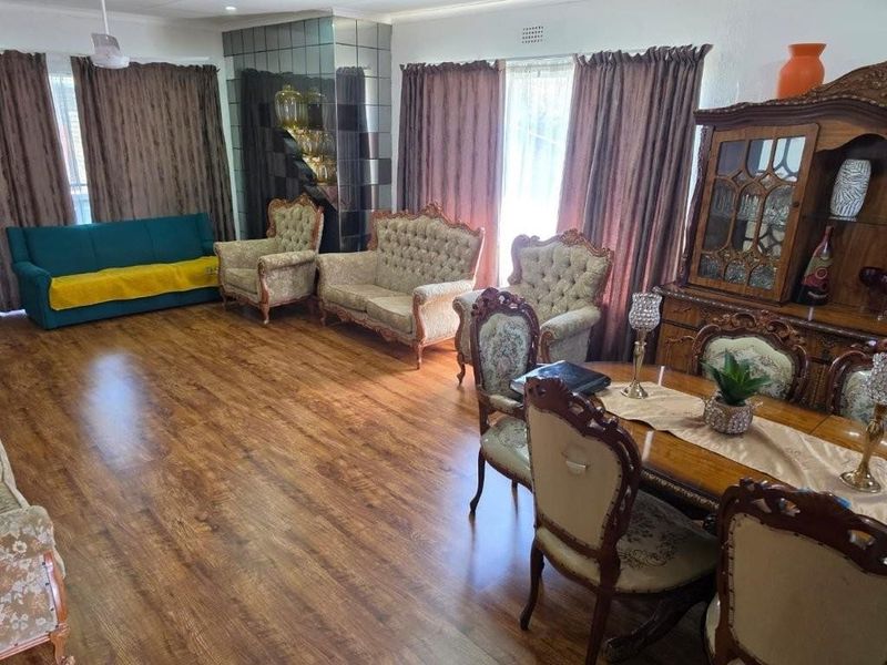 Spacious open-plan living and dining area featuring wood-look laminate flooring and a decorative mirrored feature wall.