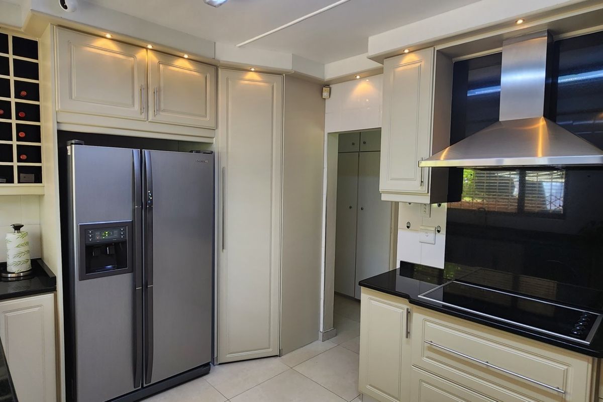 Modern kitchen featuring cream cabinetry, black granite countertops, stainless steel extractor fan, electric hob, and integrated wine storage.
