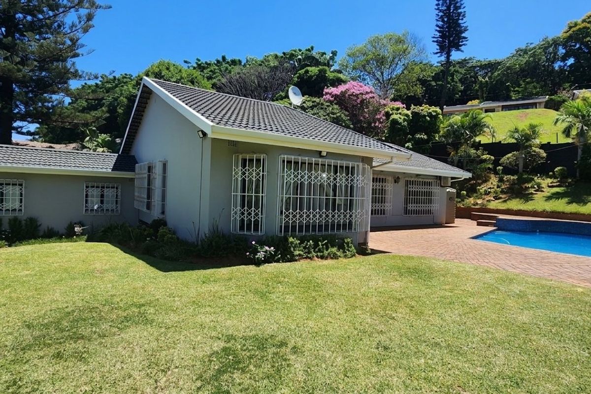 Rear view of the house featuring a well-maintained garden, paved patio area, and a swimming pool.